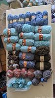 Overview of Lopi yarn skeins in light blue, teal, brown, and mixed colors laid on a white surface.