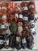 Top view of 30 skeins of assorted novelty and eyelash yarn in various colors showing texture and labels