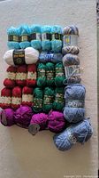 Full view of assorted yarn skeins and balls arranged by color on white surface.