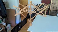 Large wooden skein winder fully expanded on white table surface.