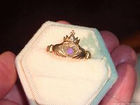 Close-up view of the gold Claddagh ring with purple stone in white ring box held by hand.