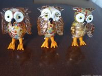 Front view of all three handmade glass owls showing different symbolic poses with multicolor glasswork and orange feet.
