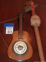 Wooden guitar-shaped barometer and toy tomahawk placed on wooden surface