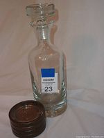 Photo of clear glass decanter with bubble base and stopper alongside brown plastic King Tut coasters stacked on their side.