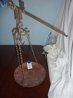 Copper and brass hanging scale with metal beam, hook, and large round copper basket suspended by chains, placed on a wooden surface.