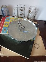 Photo showing two glass Expo '67 steins, printed materials and metal tray with spoons on it.