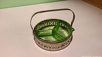 Vintage green depression glass divided dish with three sections in round metal holder with handle, photographed under regular light showing color and detail.