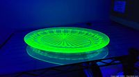 Green depression glass oval plate glowing bright green under black light, highlighting the central daisy pattern and scalloped edges.