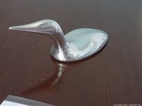 Metal loon sculpture on a wooden surface, showing the smooth reflective finish and streamlined shape.