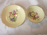 Top view of cup and saucer showing delicate sweet pea floral painting on pale yellow background with scalloped edges and gold trim