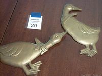 Two vintage solid brass wall mount ducks/geese on wooden surface labeled with lot number