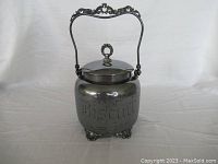 Full view of the silver plated on copper biscuit container with ornate handle and lid.