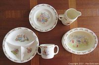 Top view showing all five pieces with Bunnykins illustrations and decorative rims on a wooden table.