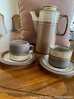 Photo of ceramic coffee set showing 2 cups each on their saucers and teapot with a speckled brown-beige glaze with banding design