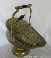 Front angle of the brass coal hod showing detailed embossed hinged lid and wooden handle.