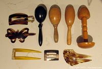 Top-down view of four wooden darning posts and four vintage hair barrettes laid out on a light background, showing details of shape, material, and color.