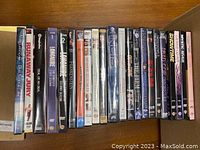 Overview photo showing 22 DVD cases lined up on a wooden surface with titles such as Runaway Jury, NCIS 2nd Season, Longmire, Frankenstein, and others visible.