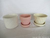 Three ceramic flower pots, pink with matched saucer and two white pots with saucers all in good condition.