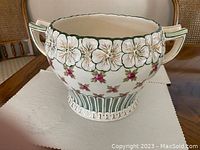 Full front view showing the floral design and handles of the jardinière on a white cloth on a wooden table.