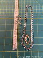 Photo showing one necklace with clear and blue rhinestones and geometric pendant, matching earrings and pin next to a ruler for size reference.