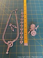 Clear crystal vintage necklace, bracelet, earrings, and pin set laid on green cutting mat with measuring ruler