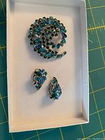Blue and green rhinestone circular brooch pin and matching clip-on earrings in white box.