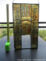 Photo showing entire stained glass panel with measuring tape for scale. Panel features rectangular design with leaded black outlines and amber stained glass with decorative motifs.