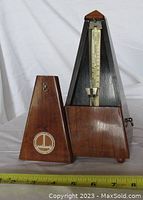 Front view of Maelzel Swiss mechanical metronome with removable wooden cover placed beside it, showing Maillard logo on cover.
