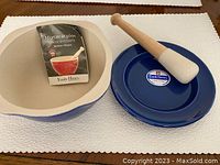 Set of Emile Henry mortar, plate, and pestle arranged on table with tag showing brand and use.