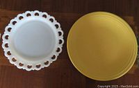 Photo showing top view of white milk glass platter with decorative edge and yellow Fiesta pottery platter side by side on wooden table.