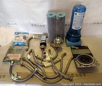Overview of water filter housing, cartridges, flexible tubes, drain strainer, and other plumbing parts arranged on a table.