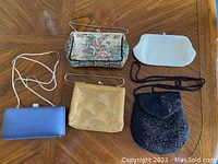 Five vintage purses of different styles and colors arranged on a wooden table.
