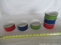 Photo showing six ramekins in red, blue, and green colors with a measuring tape showing approximately 4 inch diameter.