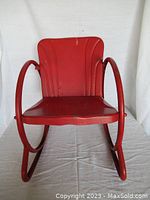 Front view of red metal child's rocking chair showing seat, back, and circular armrests with base
