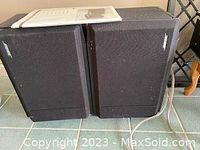 Pair of black Bose speakers placed side by side with white manual on top.