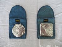 Two Birks sterling silver compacts, one round and one square, displayed on blue fabric pouches with Birks logo, showing embossed floral design.