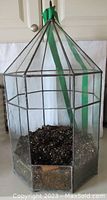 Leaded glass terrarium, hexagonal shape with metal frame and clear glass panels, soil inside, green ribbon tied on top