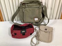 Photo showing three accessory bags against a white backdrop: green Travelon shoulder bag, red Swiss Army small bag, beige Samsonite compact bag