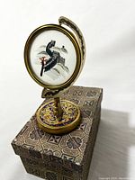 Front view of cloisonné stand with glass-covered silk embroidery depicting Asian bridge and tree.