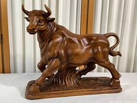 Full side view of composite wood grain painted bull figurine standing on sculpted base.