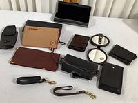 Photo showing full lot of various leather wallets, coin purses, wrist straps, and compact mirrors.