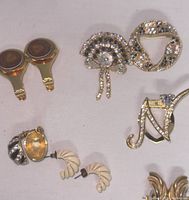Photo showing collection of brooches and two pairs of vintage earrings arranged on fabric background.