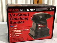 Front side of the box showing Craftsman 1/4 sheet finishing sander specifications: 1.8 amps, 14,000 orbits per minute, 1/16-inch orbit, palm grip, contents include sander, 1 sheet sandpaper, and instruction manual.