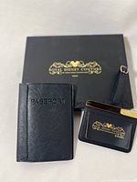 Photo showing black passport holder, small wallet, and luggage tag displayed on black box with gold 'Royal Disney Couture' logo.