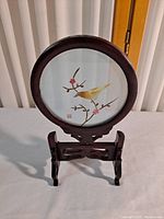 Round shadow box with yellow bird artwork and dark wood frame and stand, photo taken to show front view and details.