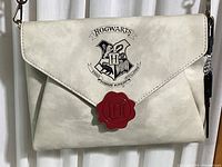 Front view of off-white leather shoulder bag featuring printed Hogwarts crest on flap and red wax seal emblem