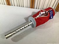 Red nylon shag bag attached to metal golf ball retriever shaft, with white golf balls visible inside the bag and attached original tag.