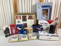 Photo showing collection of household items including boxed Fogless Shower Mirror, blood pressure monitor, router, emergency light, and 11x14 photo frame with pictures