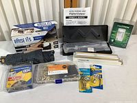 Full view of lot showing digital caliper in case with owner's manual, folding umbrella, picture hanging kits, bed raisers, LED light and Lutron dimmer switch in packaging.