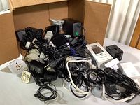 Photo showing multiple power adapters and chargers tangled and piled in a cardboard box.